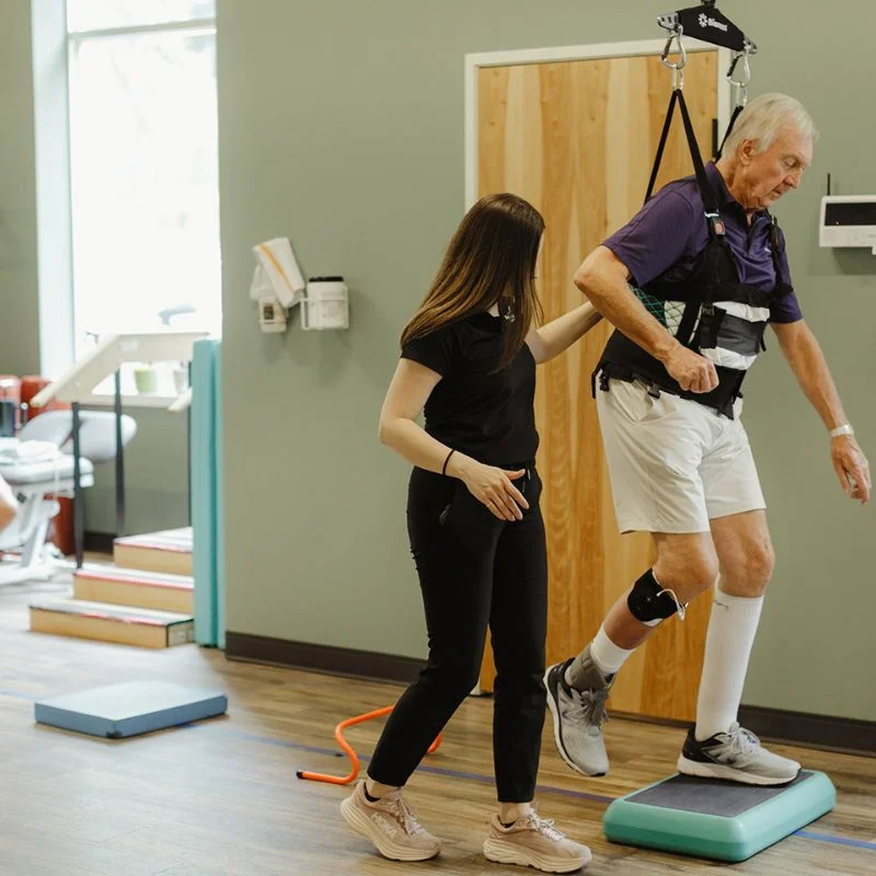 vestibular therapist supporting senior patient with harness during step balance rehabilitation in Whitby